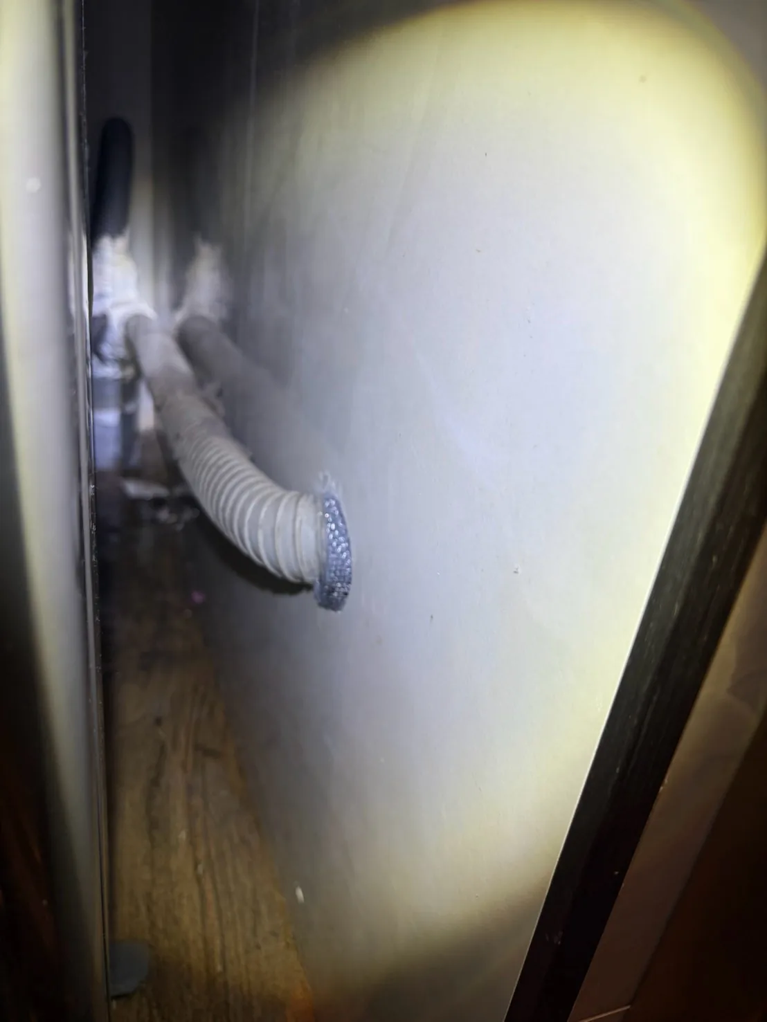 以手電筒照明檢查冷氣排水管穿牆孔，開口已用不鏽鋼網封堵